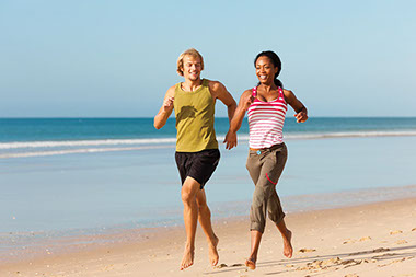 Image of young man and women jogging on the beach.