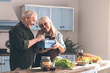 Elderly couple in kitchen, receiving gift.