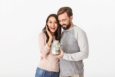 Young couple holding a jar with money in it.