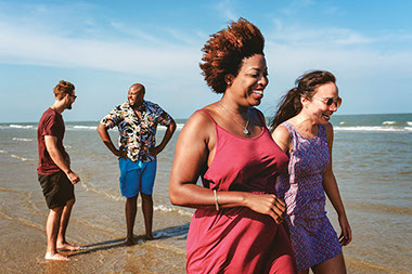 Two couples walking and laughing along the beach.