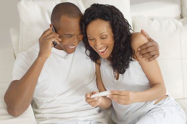 Image of happy couple looking at positive pregnancy test, while male is making a phone call.