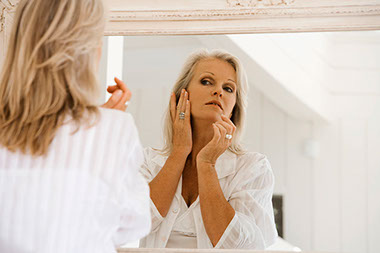 Image of women looking in a mirror examing her face.