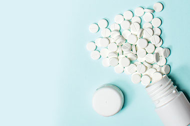 An open pill bottle with aspirin spilled out.