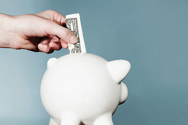 Piggy bank smarts. Image of hand placing a dollar bill into a piggy bank.