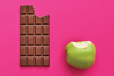 A bite out of a green apple and in a chocolate bar. A bite out of a green apple and in a chocolate bar.