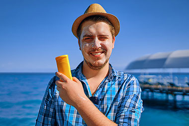 Man holding sun block in hand with sun screen on face.