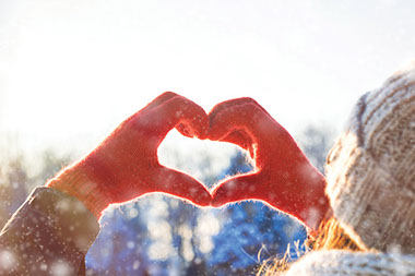 Winter image of hands wearing red gloves making a heart shape.