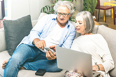Couple using laptop computer at home on sofa.