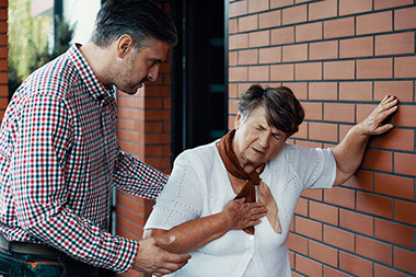 Women leaning on wall with chest pain and man helping her.