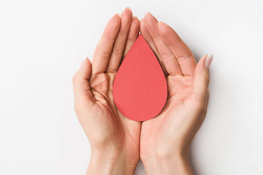 Close up of hands holding a piece of paper shaped as a blood drop.