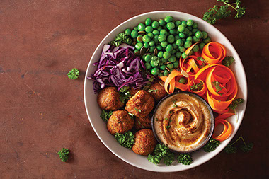 A bowl of falafel with hummus, green peas, carrots, and purple cabbage. A bowl of falafel with hummus, green peas, carrots, and purple cabbage.