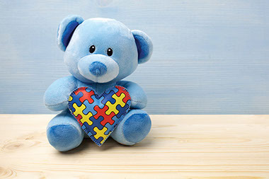 Blue teddy bear holding heart with autism puzzle icon.