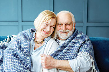 Older couple cuddling with a blanket.
