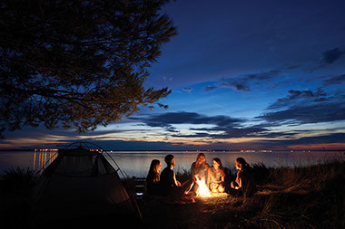 Group of people sitting around a campfire and tent.