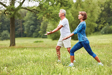 Older couple doing tai chi outside in nature.