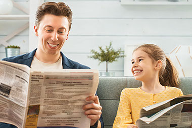 Father and daughter smiling, laughing while reading the newspaper.