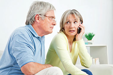 Wife on phone while husband sits besides her.