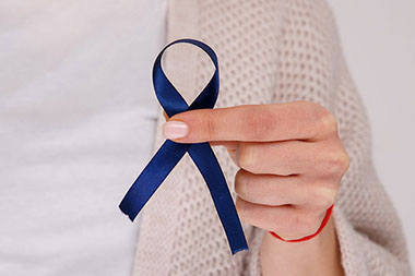Hand holding blue ribbon for colon cancer awareness.