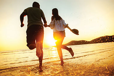Couple holding hands running into the ocean.