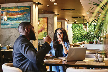 Two coworkers sitting with laptop, talking and drinking coffee.