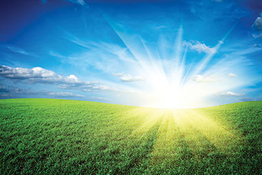 Image of sun rising behind green hills.