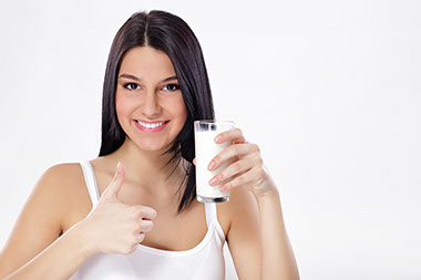 Image of teen holding a glass of milk in one hand and thumbs up with the other hand.