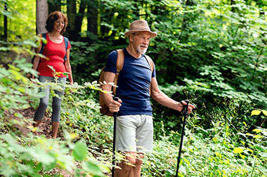 Couple hiking through trees with walking sticks.