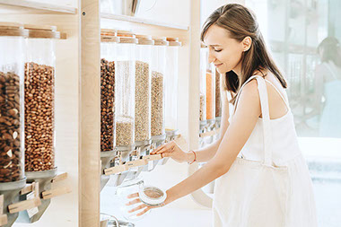 Women filling up a jar of nuts from a store's dispenser.