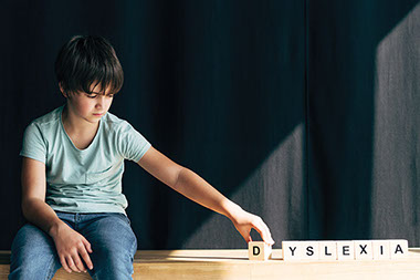 Boy spelling DYSLEXIA with wood blocks.