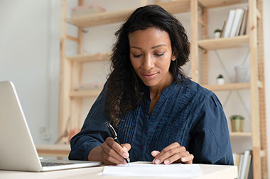 Women writing on paper with laptop next to her.