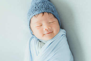 Young baby wearing blue hat and wrapped in blue blanket.