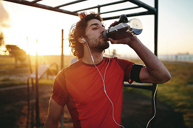 Man in workout clothes, drinking water with headphones on.