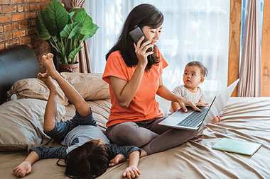 Mother on phone while using computer with 2 young children next to her. Mother on phone while using computer with 2 young children next to her.