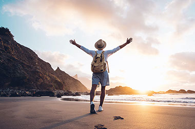 Man walking on beach with arms up in the air.