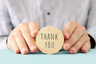 Wooden circle being held with hands with "Thank You" engraved.