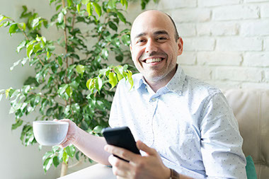 Man smiling with a cup of coffee and his phone.