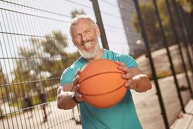 Older man smiling while holding out a basketball.