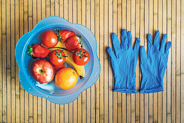 Bowl of water with fruit and vegetables and a pair of disposable gloves.
