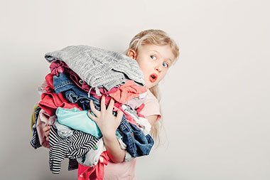 Child holding a load of clothes in her arms.