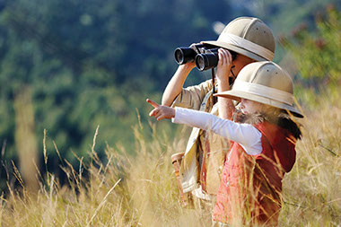 Two young kids outside with hats on looking through binoculars.