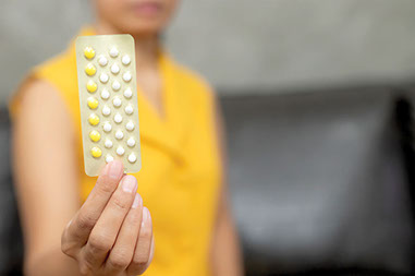 Women's hand holding up birth control pack.