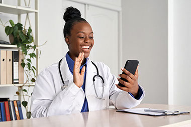 Doctor smilng and waving Hi while on a telemedicine call.