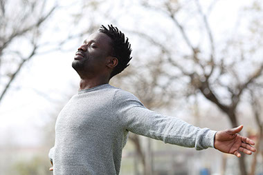 Man outside with arms open, eyes closed, breathing in the fresh air.
