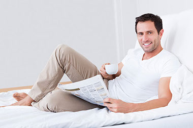 Image of man reading the newspaper in bed.