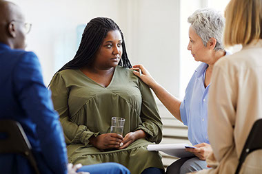 Women holding glass of water, sitting in circle with others in a support group.