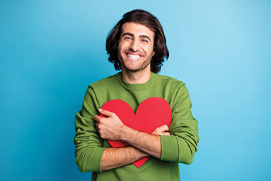 Man holding heart cut-out smiling. Man holding heart cut-out smiling.