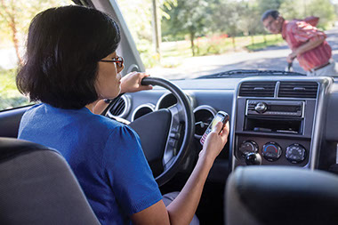 Image of women driving while looking at her phone about to hit a pedestrian.