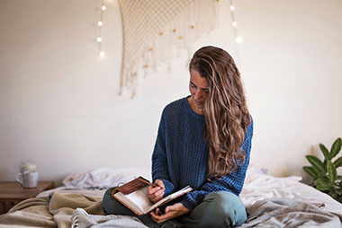 Women sitting on bed writing in journal.