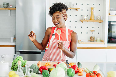 Women singing into a wooden spoon with a table filled with vegetables. Women singing into a wooden spoon with a table filled with vegetables.