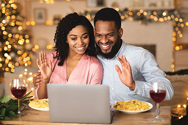 Couple waving in front of a computer screen while have dinner.